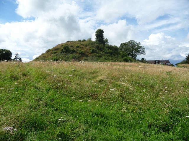Norman earthwork mound against a blue cloudy sky.